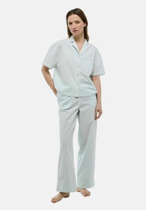 Femme debout pieds nus portant un haut de pyjama à manches courtes boutonné bleu clair et un pantalon de pyjama long assorti avec un motif à carreaux subtil.