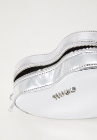 Beauty case cosmetico di colore argento, con forma curvata, doppi zip, e logo del marchio in rilievo, caratterizzato da una superficie liscia e lucida.