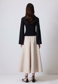 Top nero a maniche lunghe abbinato a una gonna midi beige fluida. La gonna presenta una vita arricciata e una texture liscia, completata con ballerine nere.