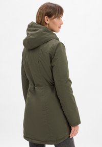Giacca con cappuccio verde oliva dal design slanciato, con vita aderente e tessuto testurizzato. Cuciture visibili e dettagli hardware minimi.