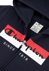 Felpa con zip blu marina, decorata con una grafica a due toni rossa e bianca sul petto con la scritta "Champion" e "SINCE 1919" in caratteri in grassetto. Dettaglio della zip in argento.