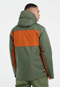 Grüne und orange wasserfeste Jacke mit Kapuze, ausgestattet mit einem großen orangen Panel über den Rücken und Logoakzenten an der Schulter und dem Saum.