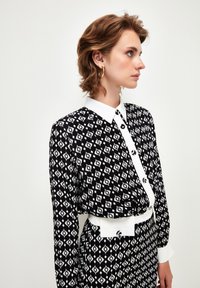 Long-sleeve dress featuring a black and white diamond pattern, a white collar, button closure, and a contrasting white belt.