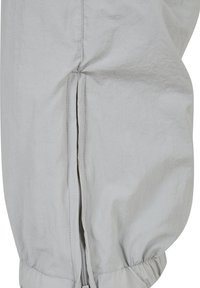 Ljusgrå jacka med texturerad tyg, elastiska ärmslut och sidodragkedja för stängning. Designen är minimalistisk och strömlinjeformad.