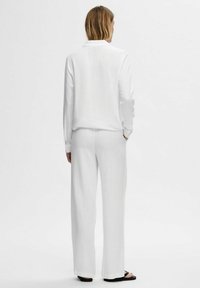 Witte linnen shirt met lange mouwen en een kraag, gecombineerd met bijpassende wijde broek, die een gladde textuur en minimalistisch ontwerp laat zien.