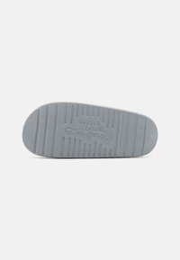 Sole di sneakers grigio chiaro con un motivo testurizzato. Caratteristiche includono creste e un logo impresso al centro, bordo della punta arrotondato e liscio.