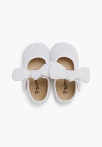 Bailarinas de tela blanca con un exterior texturizado, que presentan un gran lazo blanco en la parte frontal y una plantilla marrón con la marca "Pisamonas".