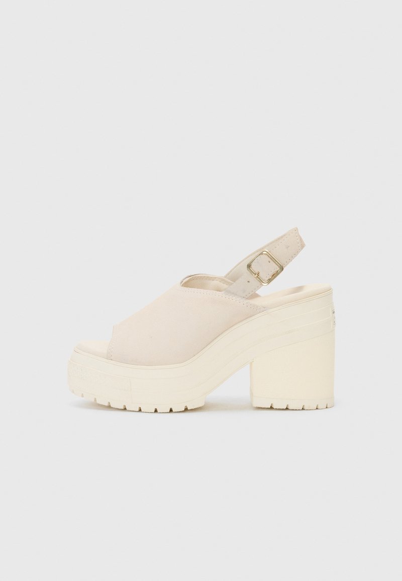 Sandale à talon plat en daim beige avec un bout ouvert, bride de cheville réglable et semelle épaisse texturée pour plus de stabilité.