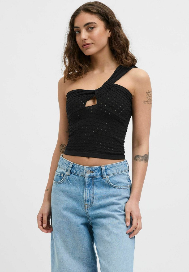 Top corto nero con design a spalla unica, tessuto testurizzato con motivi cuciti e dettaglio a forma di chiave centrale. Abbinato a jeans azzurri chiari.