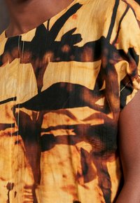 Top de manga corta en naranja y negro, con un diseño texturizado y plisado que presenta patrones abstractos y detalles de costura.