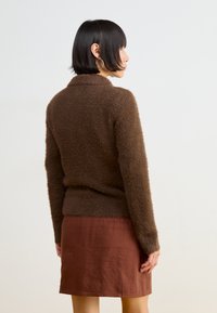 Brown fluffy sweater with a collar, paired with a rust-colored skirt. Textured fabric and long sleeves. Plain background.