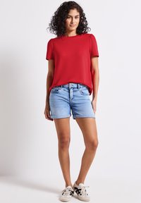 Top corto rosso a maniche corte con scollatura rotonda, abbinato a pantaloni di jeans azzurri chiari con risvolti. Indossato con sneakers bianche e nere.