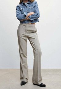 Kurtka dżinsowa z dopasowaną talią, jasnoniebieska, z dwoma kieszeniami na piersi, w połączeniu z beżowymi rozkloszowanymi spodniami i czarnymi butami z ostrym noskiem.