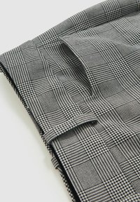 Mustvalge mustriga kangas, millel on ruuduline disain, tekstureeritud ruudud ja erineva paksusega jooned, kenasti volditud.