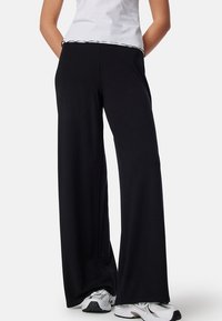Zwarte wijde broek met een gladde textuur, voorzien van een elastische tailleband en een witte accent langs de tailleband.
