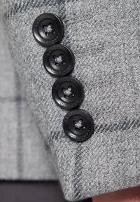 Jasnoszary, teksturowany materiał w kratkę z czterema czarnymi, okrągłymi guzikami z centralnym otworem, oznaczonymi napisem „LANCERTO.”