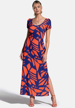 Woman wearing a navy blue and orange abstract patterned short-sleeve maxi dress with side slit and red strappy sandals.