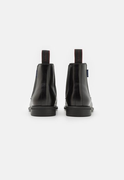 Black leather Chelsea boots with elastic side panels, round toe, low stacked heel, and contrasting red and blue pull tabs at the back.