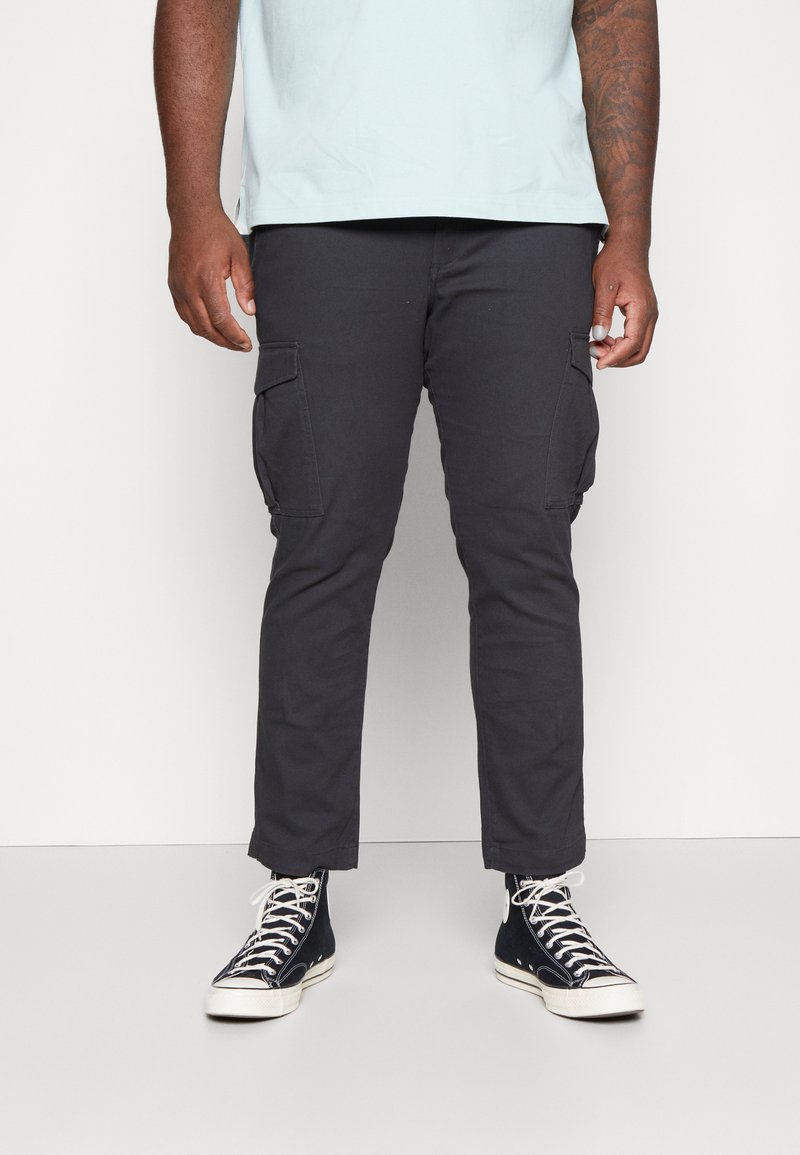 Zwarte cargobroek met zijzakken, taps toelopend ontwerp en een gladde textuur. Gecombineerd met zwarte high-top sneakers.