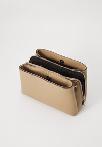 Borsa in pelle sintetica beige con due scomparti con zip. Superficie texturizzata, bordi arrotondati e interno nero. Presenta una chiusura a scatto.