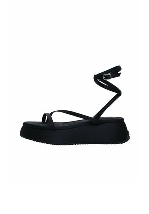 Sandali platform neri con sottili cinturini incrociati e una fascia alla caviglia regolabile. Realizzati in un materiale di gomma liscia con una suola texturizzata.