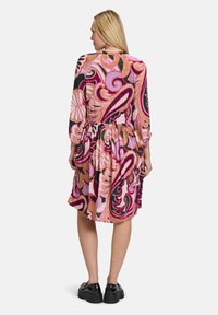 Abito con motivo floreale caratterizzato da maniche lunghe, vita arricciata e gonna svasata, nei toni di rosa, rosso e verde. Tessuto testurizzato con un design vivace.