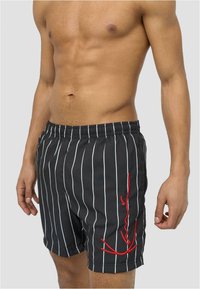 Shorts de bain rayés noirs avec des lignes verticales blanches. Équipés d'une taille élastique et d'un détail brodé rouge sur le côté gauche.