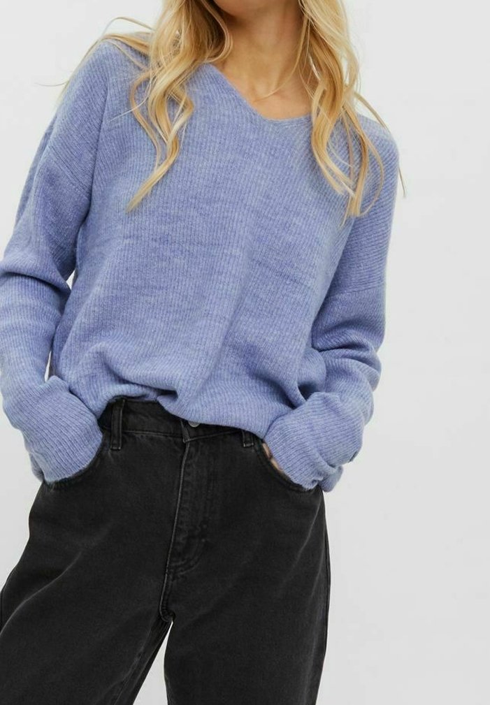 Hellblau gestreifter Strickpullover mit V-Ausschnitt, lockerer Passform und langen Ärmeln, kombiniert mit schwarzen Jeans in hoher Taille.