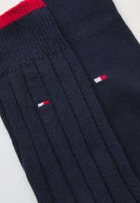 Chaussettes côtelées bleu marine avec un accent rayé rouge et blanc en haut. Présente un petit logo en rouge, blanc et bleu près du bord.