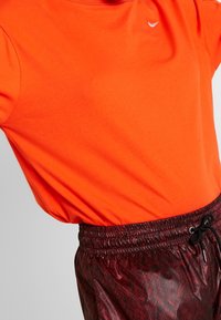 Ljusorange tröja med kort ärm och rund halsringning, matchad med mörkröda shorts med en slät, mönstrad textur och resårmidja.