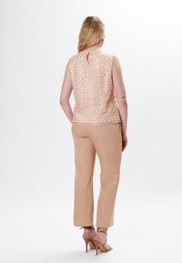 Top senza maniche di un delicato rosa chiaro con un motivo a nido d'ape testurizzato; abbinato a pantaloni beige a 3/4 e sandali con tacco color nude.