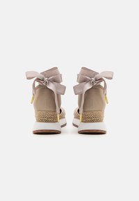 Zapatillas beige con parte superior de textil, entresuela de yute trenzado y suela de goma blanca gruesa. Presentan grandes lazos de satén en la parte posterior.