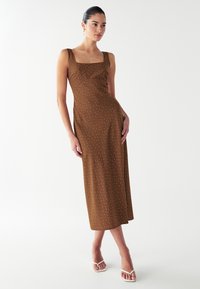 Vestido midi marrón sin mangas con escote cuadrado y lunares blancos, diseñado con un cuerpo ajustado y una falda fluida.