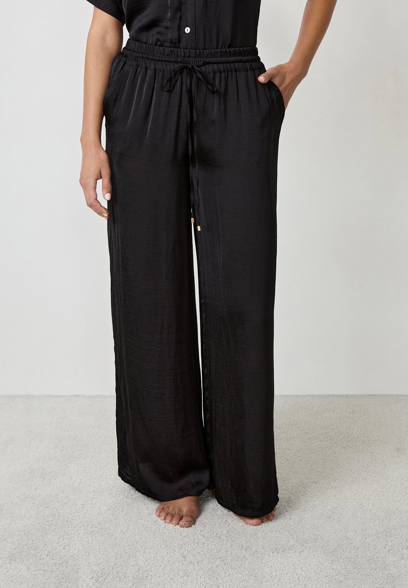 Zwarte, wijde broek gemaakt van een lichtgewicht, gladde stof. Beschikt over een elastische tailleband met een trekkoord en zijzakken.
