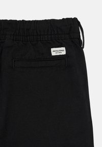 Calças pretas com um cós elástico, com um bolso na parte de trás e uma etiqueta branca com "JACK & JONES EST. 1990" visível.