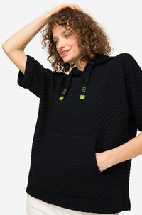 Pullover nero trapuntato con maniche corte, dotato di cappuccio e tasca frontale. Accenti verdi sui cordini, tessuto texturizzato.