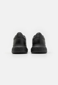 Black leather sneakers with a rounded shape, padded collar, and a textured rubber sole featuring embossed branding on the heel.