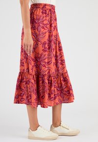 Bloemen midi rok in een levendige koraalkleur met paarse bladerenpatronen, voorzien van een elastische tailleband en een gerimpelde zoom. Geverfd met witte sneakers.