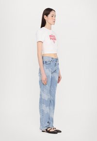 White cropped t-shirt with red print, light blue high-waisted jeans with a faded pattern, and black flat shoes with a decorative strap.