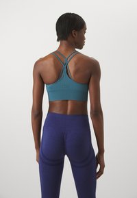 Sujetador deportivo de color aguamarina con tirantes cruzados, combinado con leggings de un azul profundo que presentan una textura recogida y acentos de rayas en curva.