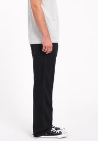 Sorte jeans med et lige ben-design, der har sidelommer og baglommer. Båret med sort og hvidt sneakers.