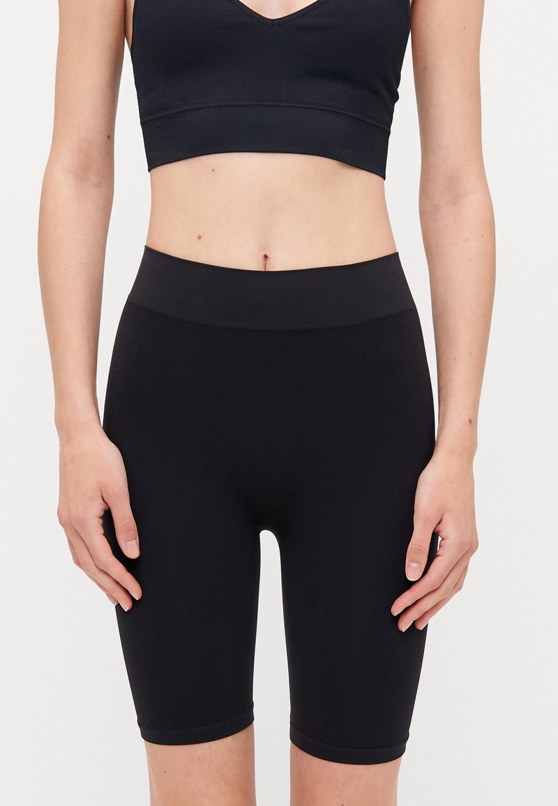 Black bike shorts made of stretchy fabric, featuring a high waistband and knee-length cut, smooth texture with no visible patterns or accents.