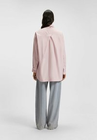 Light pink long-sleeved shirt with a back pleat, featuring a pointed collar and button cuffs. Paired with wide-leg light gray trousers.
