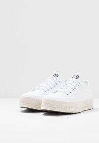 Sneaker bianche in tela con una piattaforma in juta intrecciata e texturizzata. Presentano occhielli metallici e lacci bianchi piatti. Logo nero sulla linguetta.