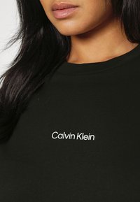 Svart bomullströja med rund halsringning och vit text "Calvin Klein" tryckt på bröstet. Kort ärm-design.