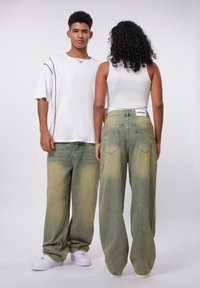 Baggy grønne denimjeans med et falmet design, med store baklommer og en merket midje. Kombinert med en hvit topp og sneakers.