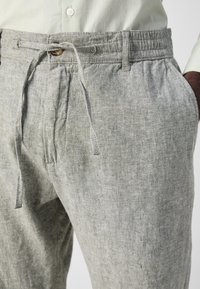 Pantalons en lin gris clair avec une taille élastique, un cordon de serrage et deux poches latérales, en tissu texturé et respirant.