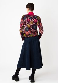 Flerfärgad blommig tröja med rosa krage, i kombination med en mörk denimkjol. Modellen bär svarta knästrumpor och platåskor.