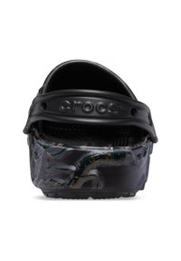 Zwarte Crocs met een gestructureerde, patroonachtige buitenkant met groene en gele accenten, ontworpen voor comfort met een brede, verstelbare band.