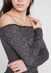 Schwarz-graues Off-Shoulder-Oberteil mit strukturiertem, gerafftem Stoff und langen Ärmeln, das ein dezentes Muster durchgehend aufweist.